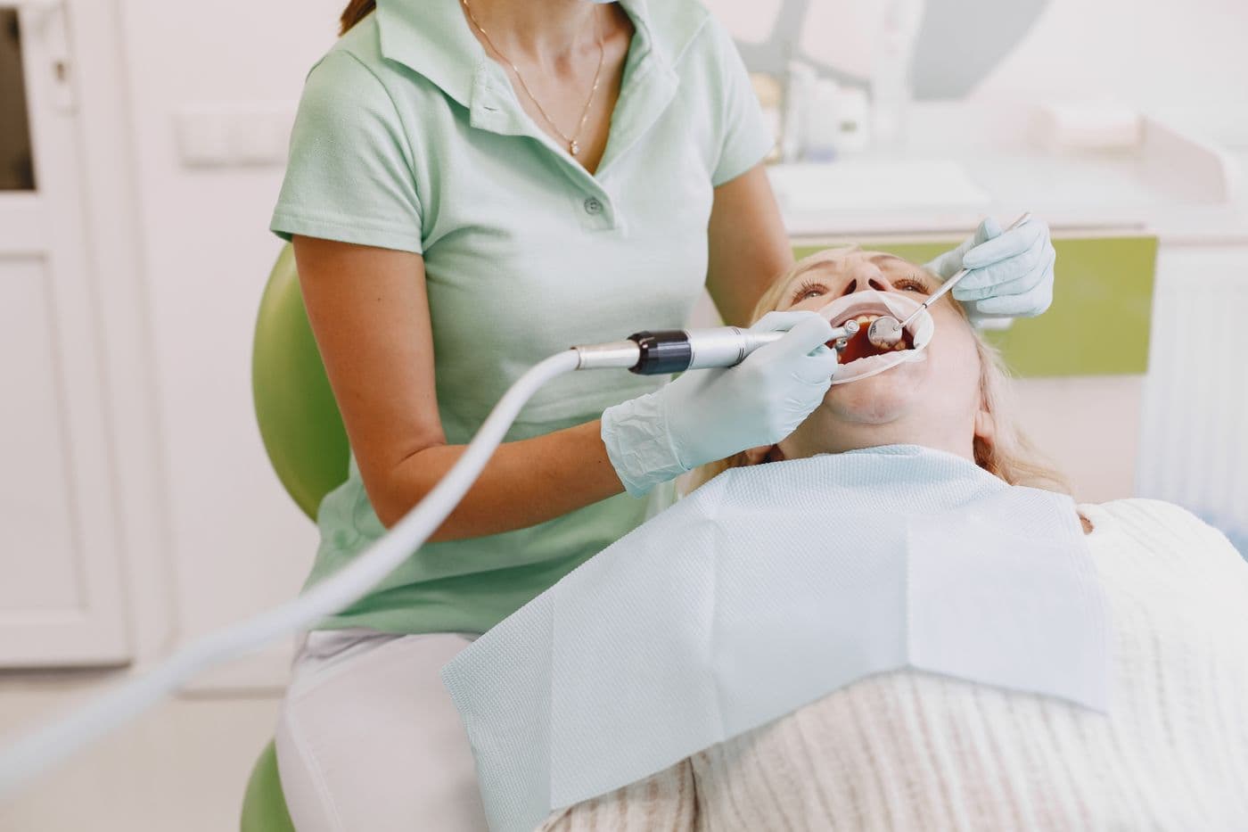Dental hygienist cleaning a patient's teeth with the patient reclined in the chair