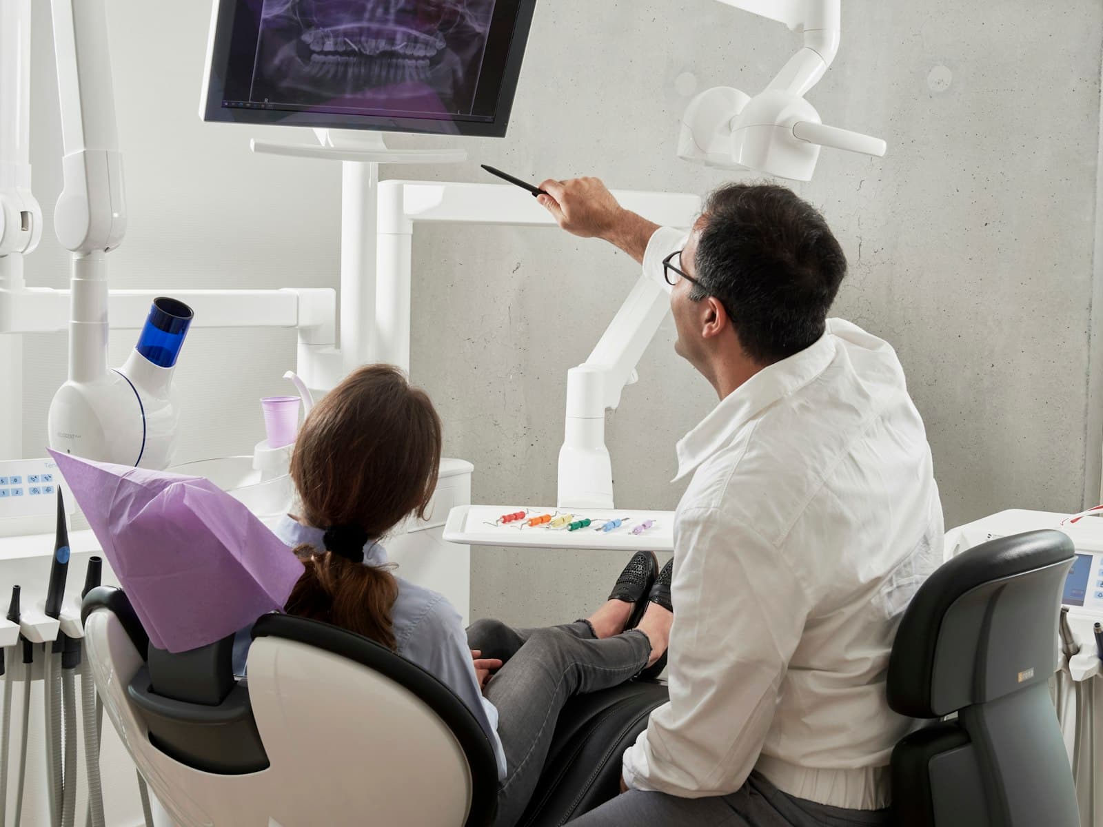 Dentist pointing at a dental scan on screen while explaining it to a patient