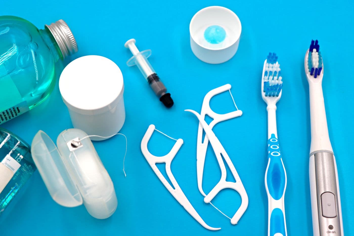 Toothbrushes, floss picks, floss and mouthwash laid out on a blue background