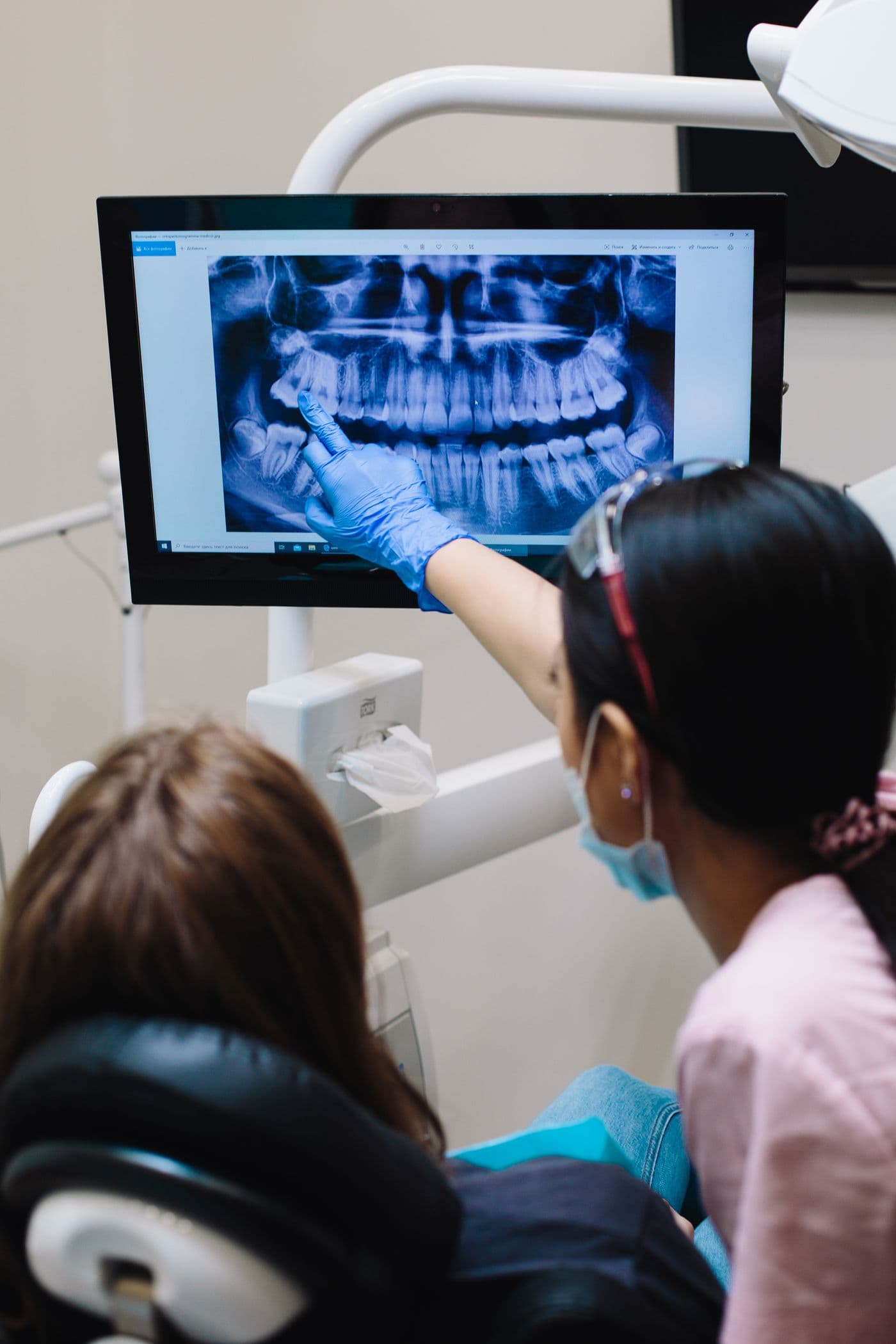 Dentist pointing at a wisdom tooth on a panoramic X-ray while a patient looks on
