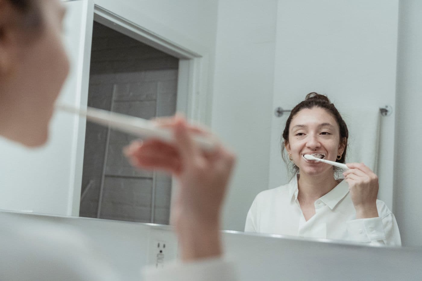 Woman brushing her teeth gently in a bathroom mirror